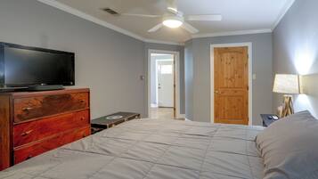 A bedroom with a bed, dresser, television, ceiling fan, and a door leading to another room.