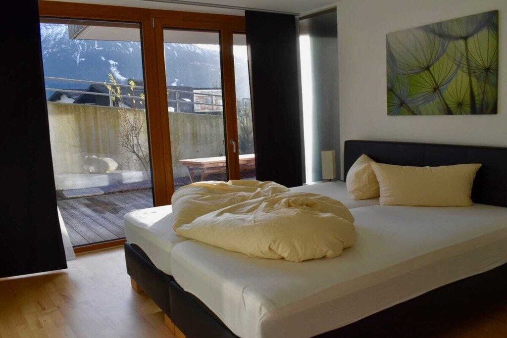 A bedroom with a bed, a window, and a view of a balcony.