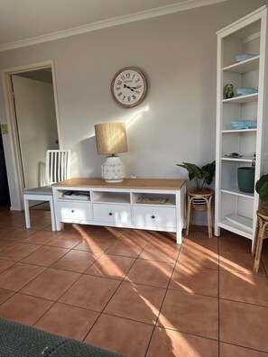 Ein Zimmer mit einem weißen Konsolentisch, einer Uhr, einer Lampe, einem Stuhl und einem weißen Regal.