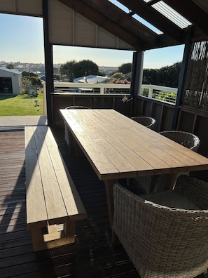 Eine Terrasse im Freien mit einem Holztisch und Korbstühlen, mit Blick auf ein Wohngebiet.