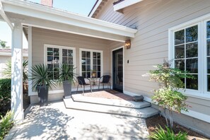 A covered patio with a brick floor, two chairs, and potted plants. - Luxury Manhattan Beach Home in Parklike Gated Community (Manhattan Beach)