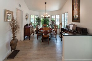 A dining area with a piano, wooden chairs, a chandelier, and potted plants. - Luxury Manhattan Beach Home in Parklike Gated Community (Manhattan Beach)