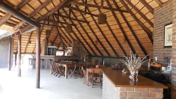 Une cuisine à aire ouverte avec un comptoir en briques, des tabourets en bois et un toit de chaume.