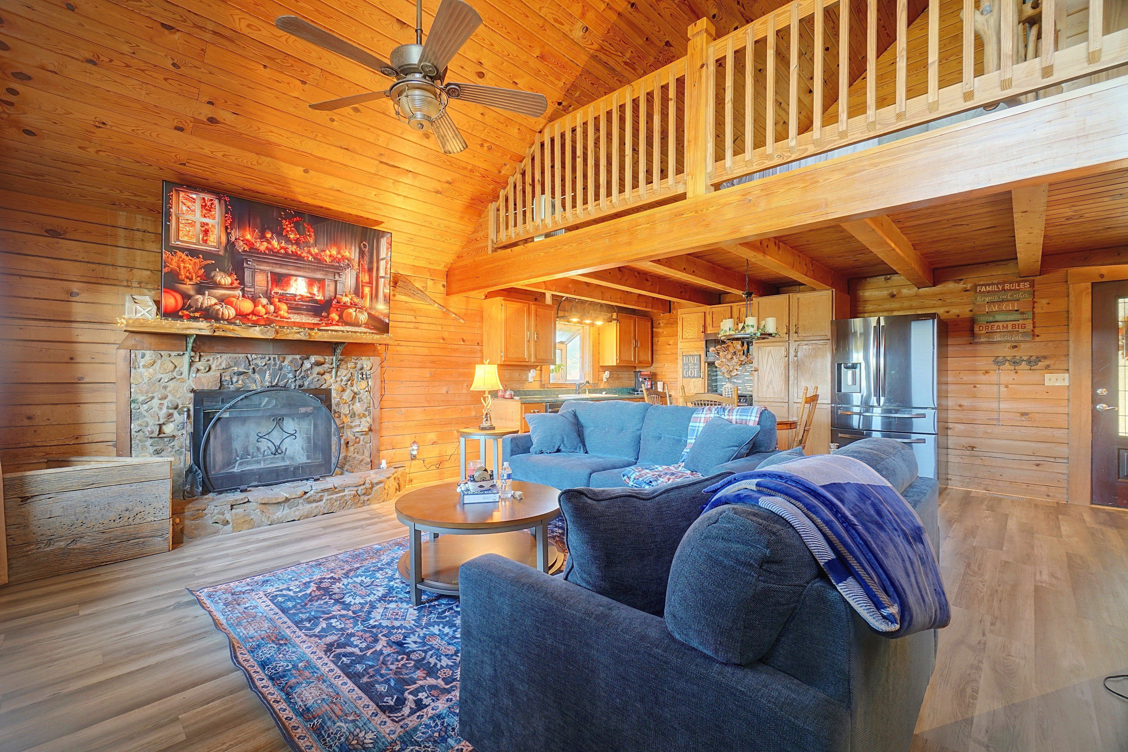 A cozy cabin interior with a fireplace, a dining area, and a living room furnished with a sofa and armchairs.