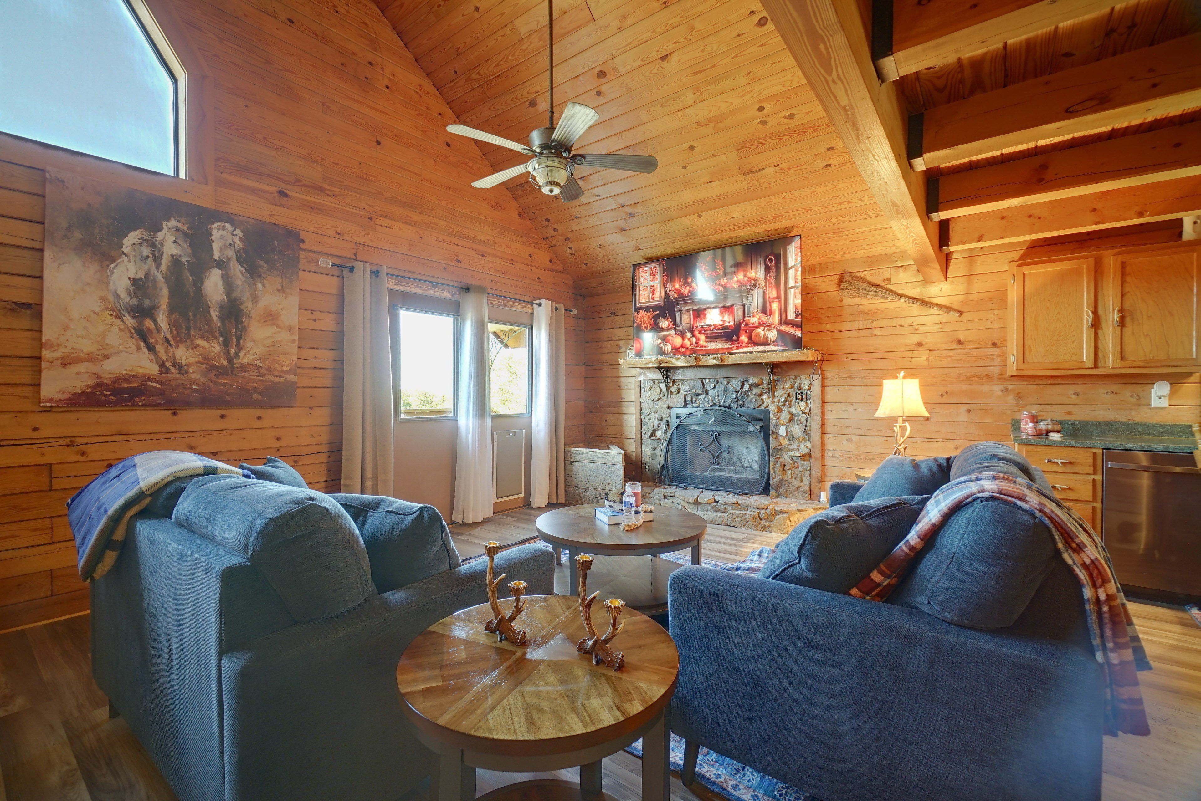 A cozy cabin interior with a fireplace, wooden walls, and a ceiling fan.