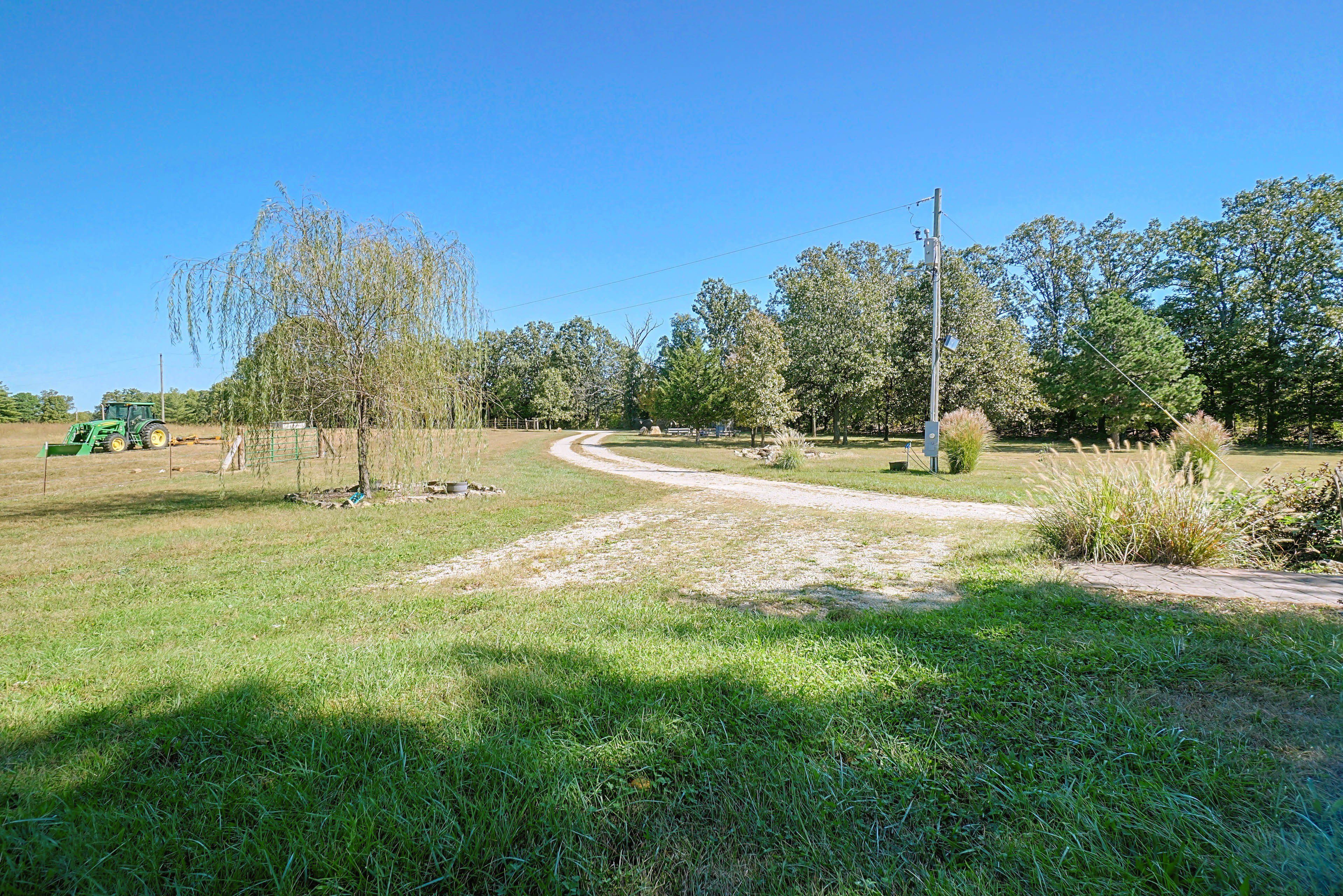 A rural landscape with a dirt path, green grass, and trees.