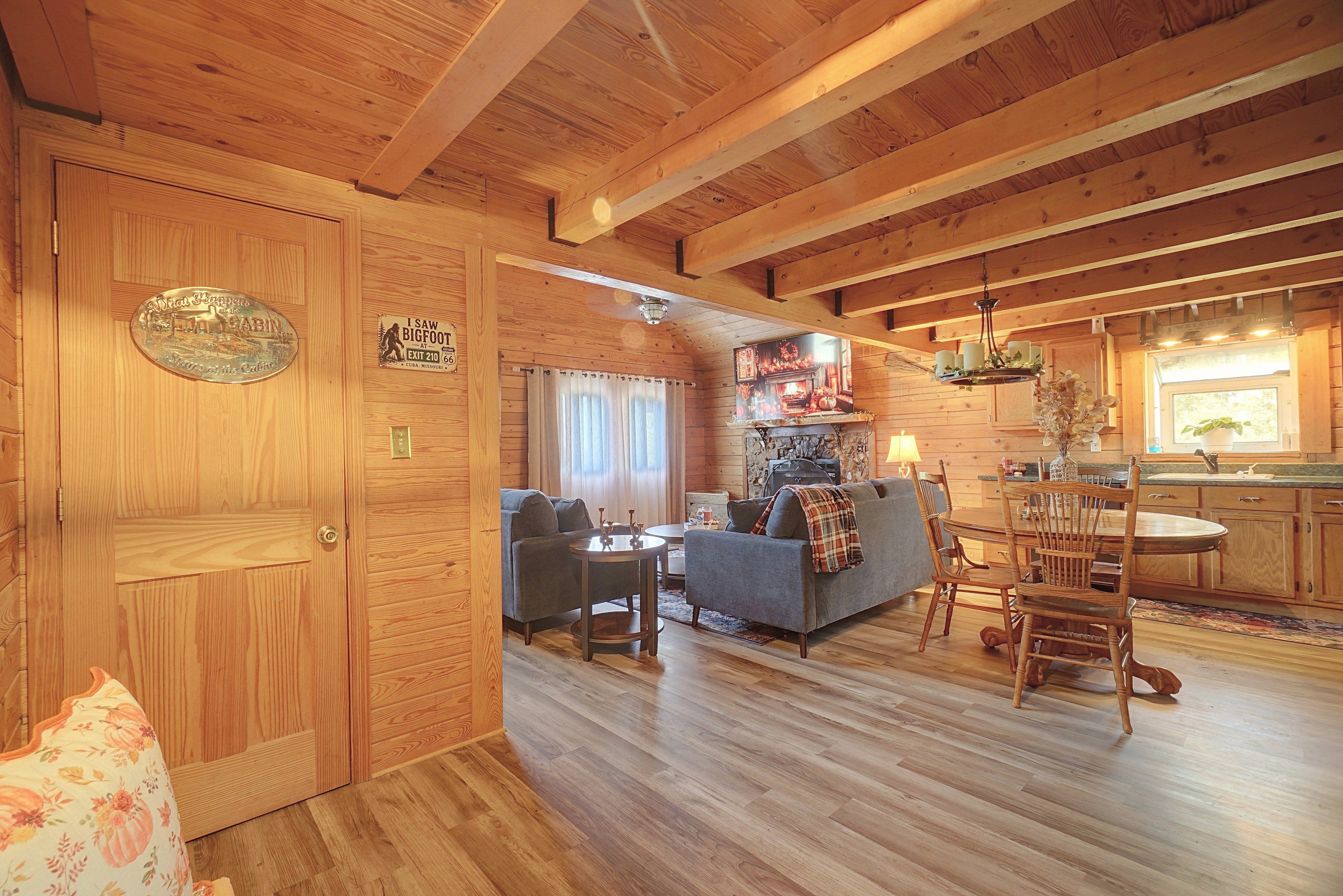 A cabin interior with a wooden floor, a sofa, a dining table, and a kitchen area.