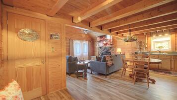 A cabin interior with a wooden floor, a sofa, a dining table, and a kitchen area.