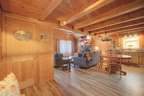 Ein Interieur einer Holzhütte mit Holzboden, einer Couch, einem Esstisch und einer Küchenzeile.