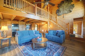 A spacious log cabin interior with a high ceiling, a staircase, a dining area, and a kitchen.