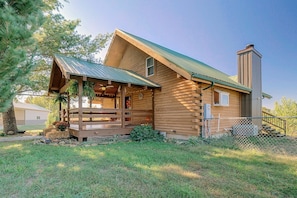 A log cabin with a porch, a chimney, and a fenced yard.