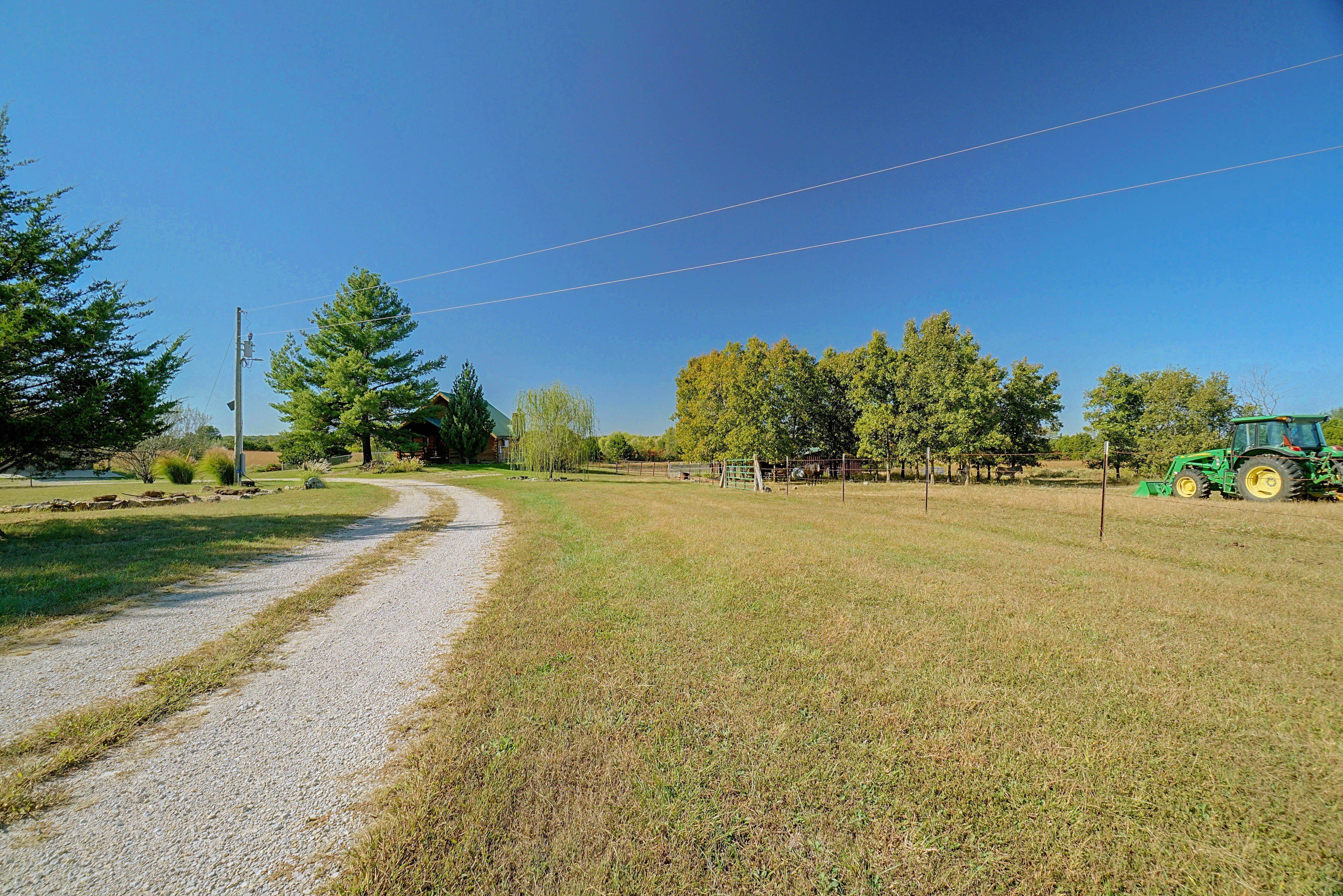 A rural landscape with a gravel path, trees, and a green tractor.