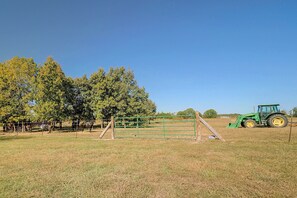 A rural landscape with a green tractor, a fenced area, and trees.