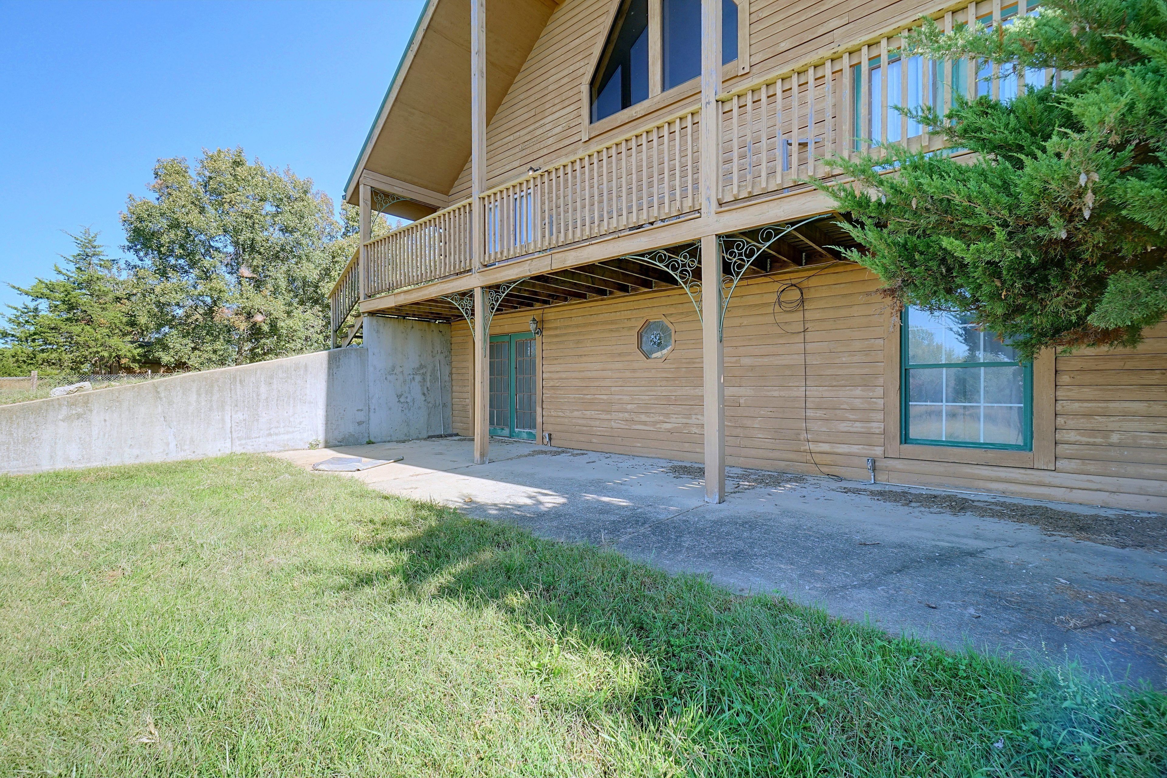 A two-story wooden building with a balcony, a concrete wall, and a grassy area.
