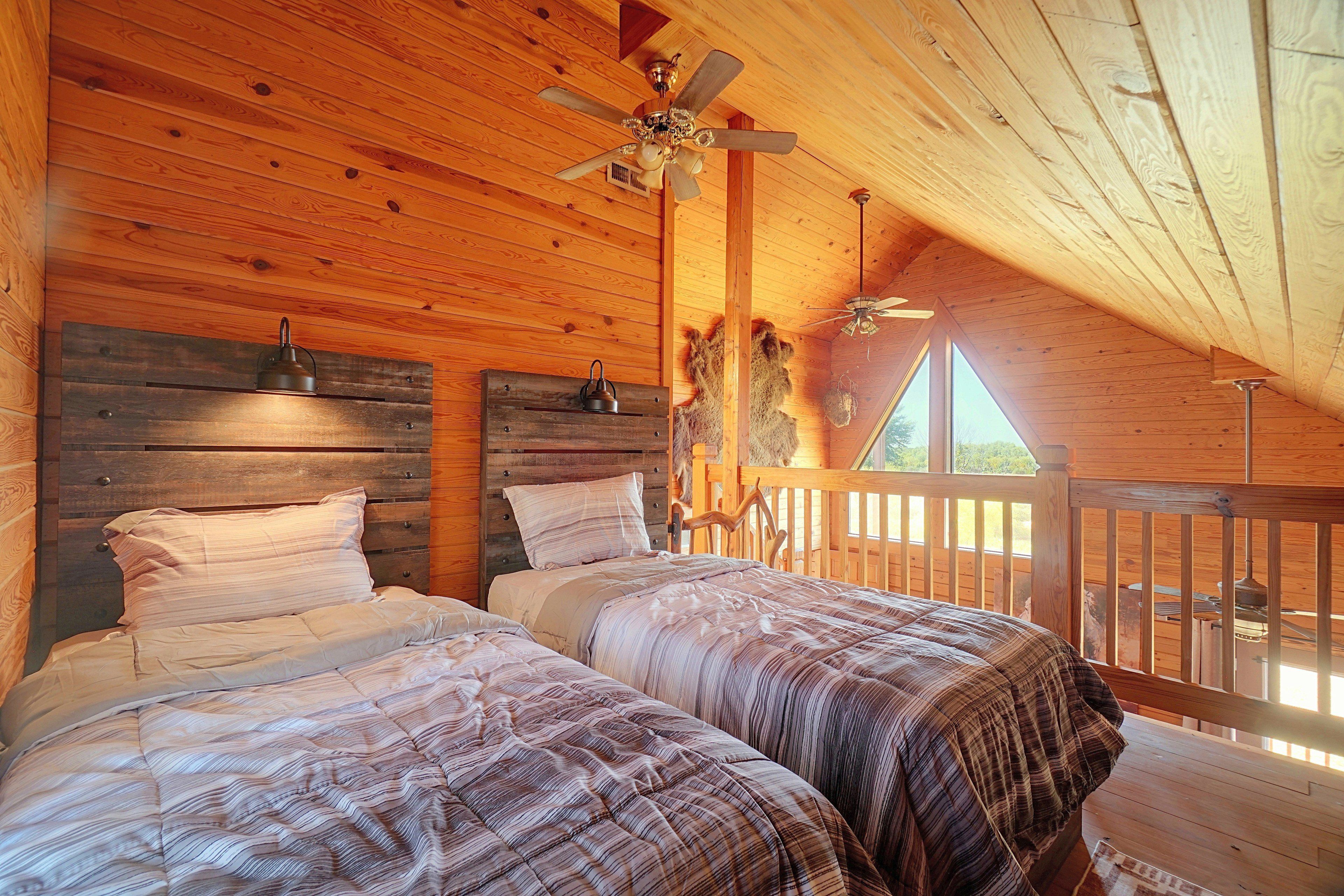 Une chambre dans une cabane en bois, avec deux lits, un ventilateur de plafond et une fenêtre donnant sur une terrasse.