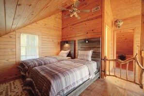 A wooden cabin bedroom with two beds, a ceiling fan, and a rustic wooden door.