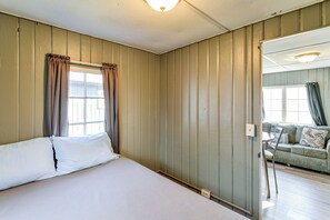A hotel room with a bed, a window with curtains, a mirror, and a view of a living area. - Direct Shoreline Access! Tawas City Cabin (Tawas City)