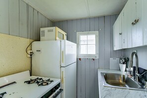Eine kleine Küche mit einem Gaskochfeld, einem weißen Kühlschrank, einer Mikrowelle und einem Spülbecken mit Armatur.