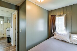 Una camera da letto con un letto, una finestra con tende, una porta e un angolo cottura.