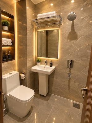 A modern bathroom with a toilet, sink, and shower. There is a towel rack above the sink and a mirror above the toilet. - Hotel Empire Inn  (Varanasi)