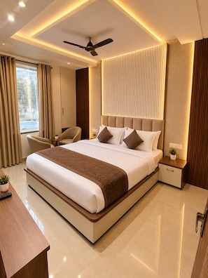 A modern hotel room with a large bed, a ceiling fan, a desk, and a view of the outdoors. - Hotel Empire Inn  (Varanasi)