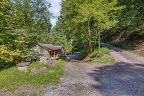 A rustic cabin with a stone wall and wooden roof, surrounded by dense forest and a gravel path. - Rustic Cabin Retreat in the Peaceful Mountains (Elk Park)