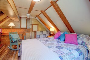 A bedroom with a sloped ceiling, wooden beams, a bed with a quilt, a chair, a desk, and a lamp. - Norfork Lake Cabin, 2 Mi to the Water (Jordan)