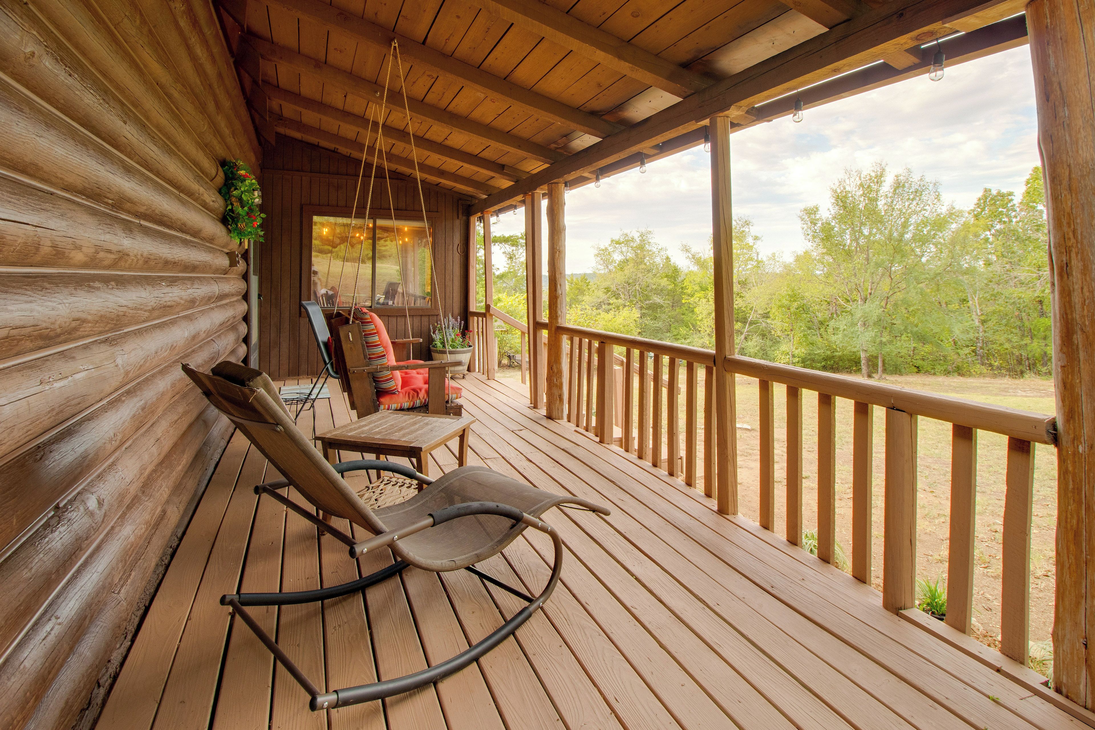 Une terrasse en bois avec un fauteuil à bascule, une table et une balançoire suspendue.