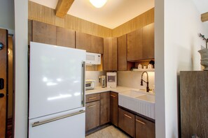 A kitchen with wooden cabinets, a white refrigerator, a microwave, a toaster, and a sink with a modern faucet. - Mid-Century Modern Chateau du Coach House (Iowa City)