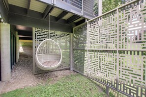 A hanging chair in a covered outdoor area with a decorative fence. - Mid-Century Modern Chateau du Coach House (Iowa City)