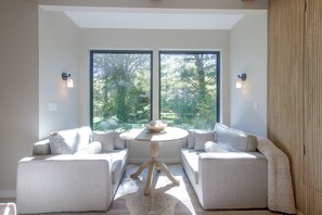 Una habitación con dos sofás orientados hacia una mesa, ventanas amplias y luces fijadas a la pared.