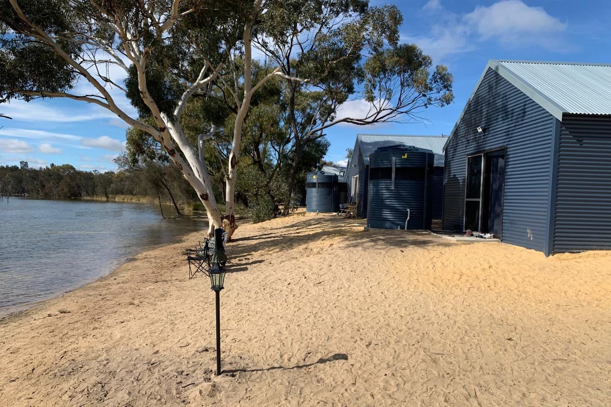 A sandy beach with a metal structure and a tree.