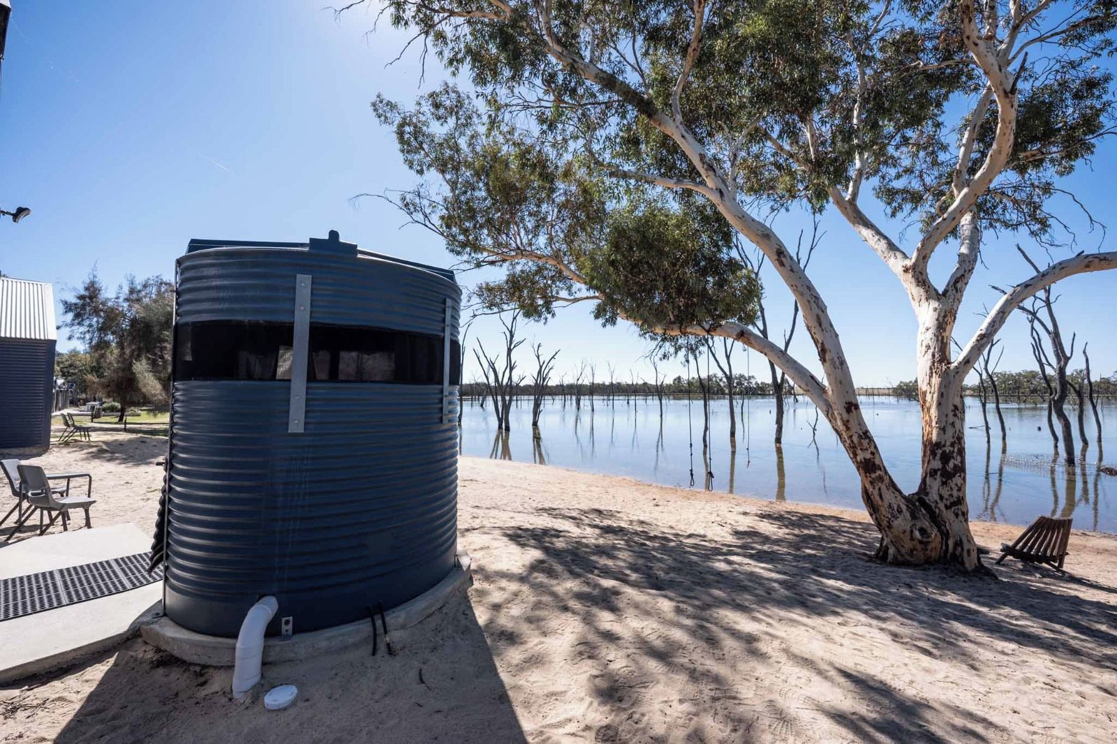 Un serbatoio d'acqua, una spiaggia sabbiosa e un albero vicino all'acqua.