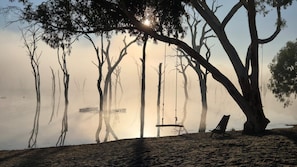 A beach with a swing, trees, and a calm body of water.