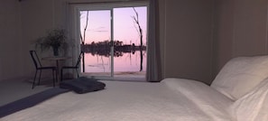 Una camera da letto con un letto grande, una sedia, un tavolino e vista su un lago tramite una porta scorrevole.