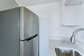 Un refrigerador de acero inoxidable en una cocina con encimera blanca y un lavamanos.