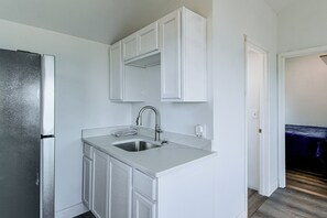 A kitchen with a stainless steel sink, white cabinets, and a door leading to a bedroom. - Yard w/ Lake Views! Quaint Tawas City Escape (Tawas City)