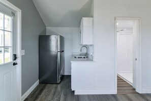 Una cocina compacta con refrigerador, lavamanos y muebles de color blanco.