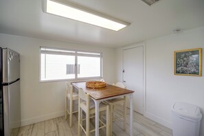 A compact kitchen with a refrigerator, a dining table with chairs, a window with blinds, and a wall-mounted trash bin. - Walk to the Beach! Bright Cape Canaveral Apt (Cape Canaveral)