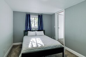Ein Schlafzimmer mit einem Bett, einem Fenster mit Vorhängen und einer Tür.