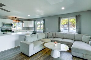 A modern living room with a sectional sofa, a round coffee table, and a kitchen area with appliances. - Lakefront Tawas City Gem w/ Gazebo & Beach Access (Tawas City)