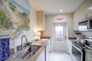 A modern kitchen with stainless steel appliances, a sink, and a painting on the wall. - Cape Canaveral Getaway w/ Pool - Walk to Beach (Cape Canaveral)