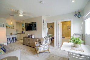A spacious living area with a wooden floor, a dining table, a sofa, and a TV mounted on the wall. - Cape Canaveral Getaway w/ Pool - Walk to Beach (Cape Canaveral)