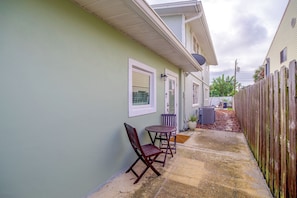 A narrow outdoor patio with a table and chairs, a wooden fence, and a building with a light green exterior. - Cape Canaveral Getaway w/ Pool - Walk to Beach (Cape Canaveral)