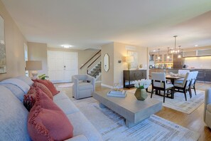 Una sala de estar moderna con un sofá, sillones, una mesa de centro y un comedor con sillas y una mesa.