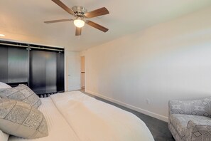 Une chambre à coucher avec un lit, un ventilateur de plafond, une armoire et une chaise à motifs.