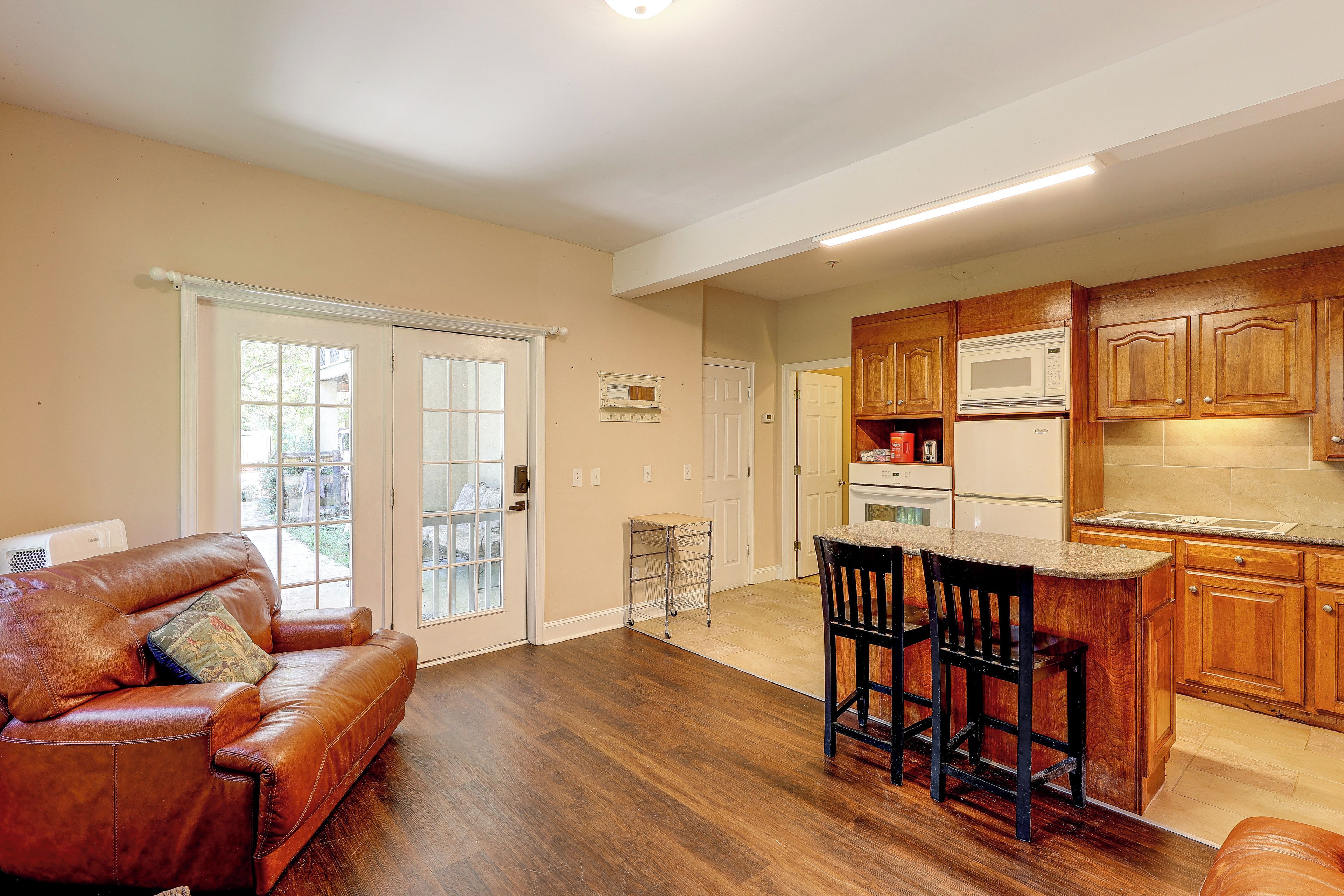 A spacious living room with a brown leather sofa and a dining area with bar stools.