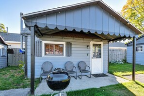A small, single-story building with a porch, a barbecue grill, and three chairs. - Quaint Couple’s Unit w/ Lake Access in Tawas City (Tawas City)