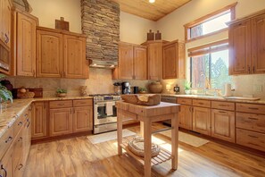 A spacious kitchen with wooden cabinets, a stone accent wall, and a large window providing natural light. - Golf Course Days, Fireside Nights! Show Low Escape (Show Low)