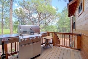 Ein Weber-Gasgrill auf einer Holzterrasse mit Blick auf einen Wald.